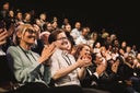 Happy colleagues applauding while sitting in conference event at convention center
