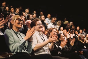 Happy colleagues applauding while sitting in conference event at convention center