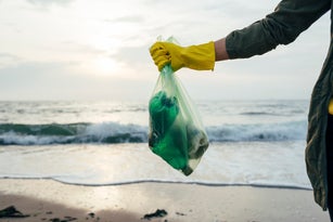 Mid adult woman holding garbage bag while standing at beach