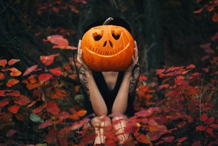 The girl sits in the forest and holds a pumpkin in her hands. Halloween pumpkin. Autumn background.