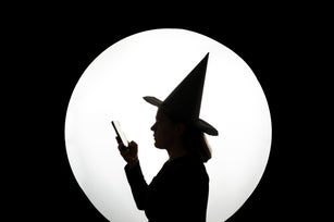 Silhouette of witch in hat with large full moon and smartphone