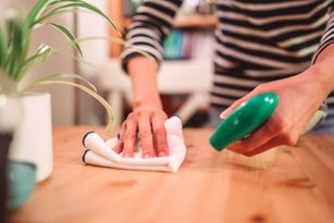 Close-up of woman hands cleaning the surface of a table with disinfectant spray & cloth at home