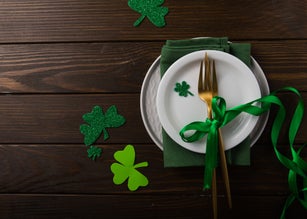 St. Patrick's Day green Shamrocks with fork, spoon, and napkin on rustic brown wood board background with room or space for copy, text, words. Square