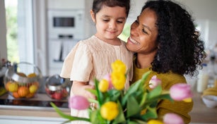 Multiracial girl giving flowers her mother in their kitchen, having fun.