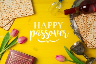 Jewish holiday Passover Pesah celebration with matzoh, tulip flowers and wine bottle on yellow wooden background. View from above