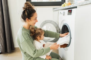 Mother and child girl little helper loading washing machine.