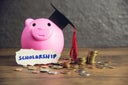 Close-Up Of Scholarship Text With Piggy Bank And Coins On Table