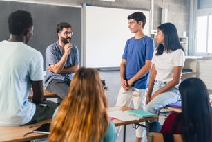 Group of teenagers and male teacher at classroom talking and discussing together
