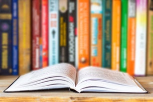 Close-up of opened book on bookshelf on blurred books background. Home library reading books concept