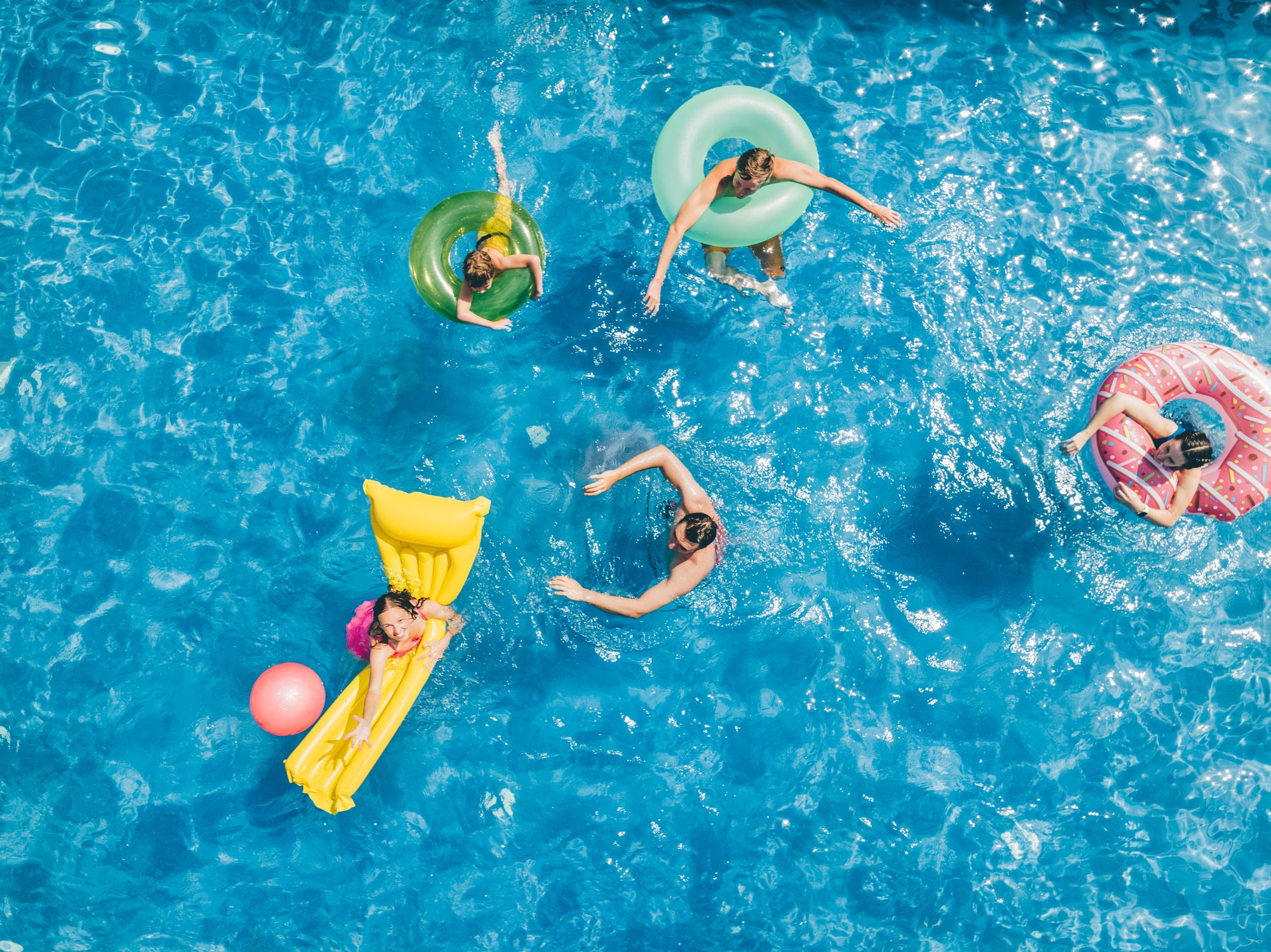 Friends having fun while playing with ball in the swimming pool.  Aerial view.
