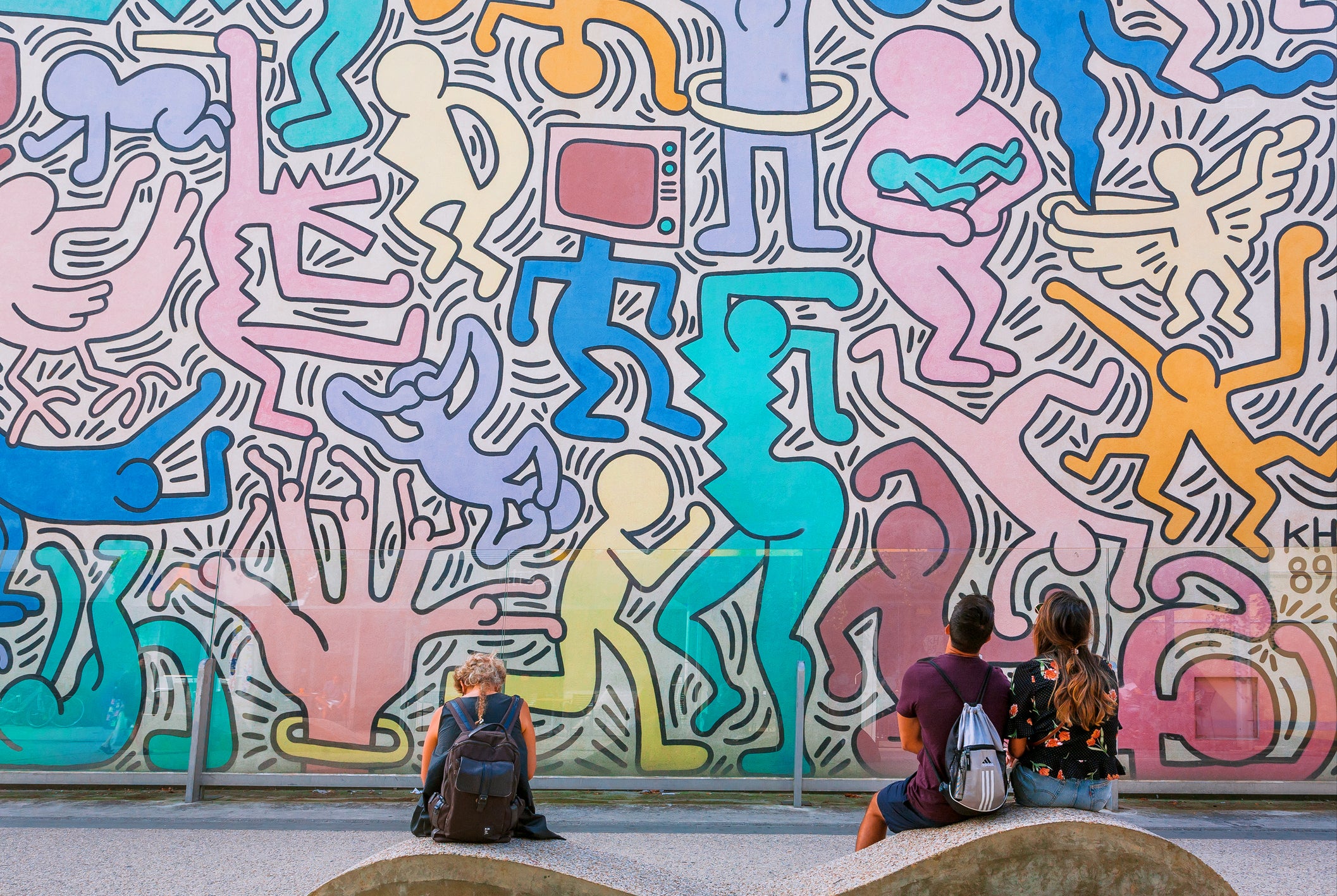 People watching on wall with artwork by modern artist Keith Haring, famous in pop-art style
