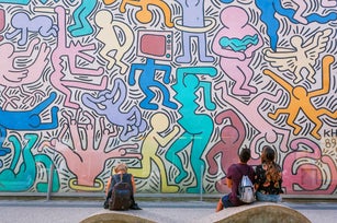 People watching on wall with artwork by modern artist Keith Haring, famous in pop-art style