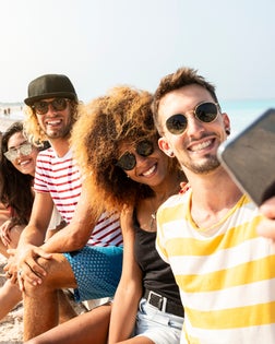 Friends sitting on the beach, having fun, taking selfies