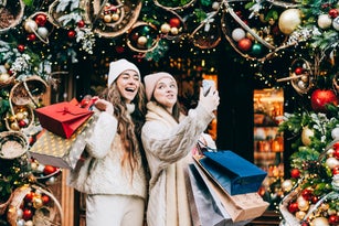 Two girlfriends enjoying Christmas shopping, making funy faces, taking a selfie for their friends
