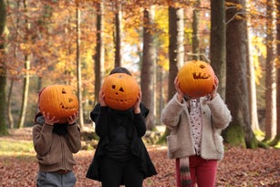 Children covering their faces with carved pumpkins.