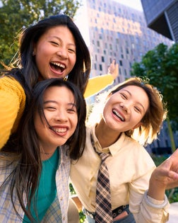 Three female friends taking a cheerful selfie outdoors in the city, doing piggyback.