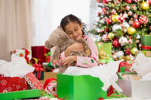 Hispanic girl hugging teddy bear Christmas gift