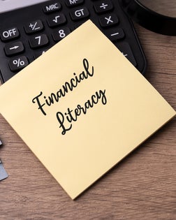 Financial Literacy Text on Adhesive Note With Calculator, Magnifying Glass and Paper Currency