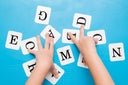 Girl's hands touching white cards of letters for little kids on the blue table. Time to learn. Education concept. Top view.