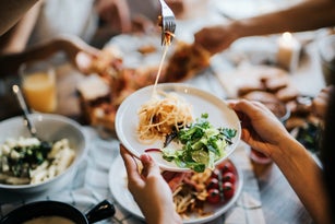 Group of joyful young Asian man and woman having fun, passing and sharing food across table during party