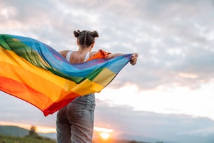 diversity Girl standing back and holding rainbow flag on sky background