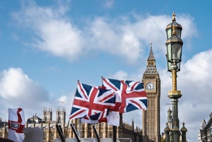 View of Big Ben tower and a lamp post on Westminster Bridge on a sunny day against blue sky with Union Jack flags at the forefront