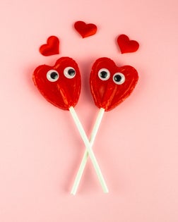 Concept of love and romanticism. Two red heart lollipops with eyes looking at each other and several red hearts