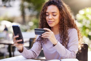 Shot of a young woman using a credit card and phone at a cafe