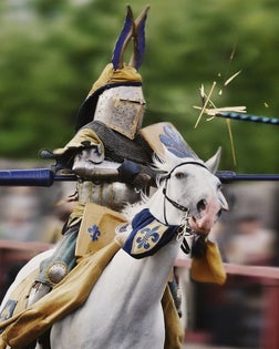 Man participating in jousting tournament, lance impacting on shield