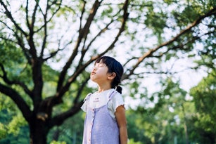 Lovely little Asian girl breathing fresh air with eyes closed in the nature. Enjoying nature with clean air in park. Childhood lifestyle. Carefree and freedom. Connect with the nature concept