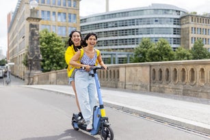Portrait of two cheerful  women friends on holiday having fun on push scooter in city