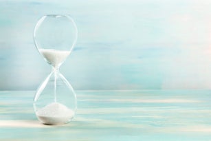 A side view of an hourglass with falling sand, on a teal background with copy space