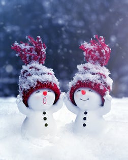 Two little snowmen in caps on snow in the winter. Background with a funny snowman. Christmas card.