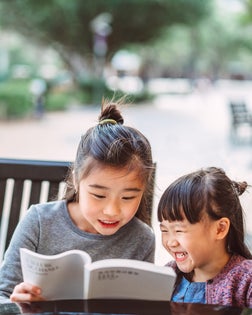 Little sibling reading storybook joyfully at outdoor cafe