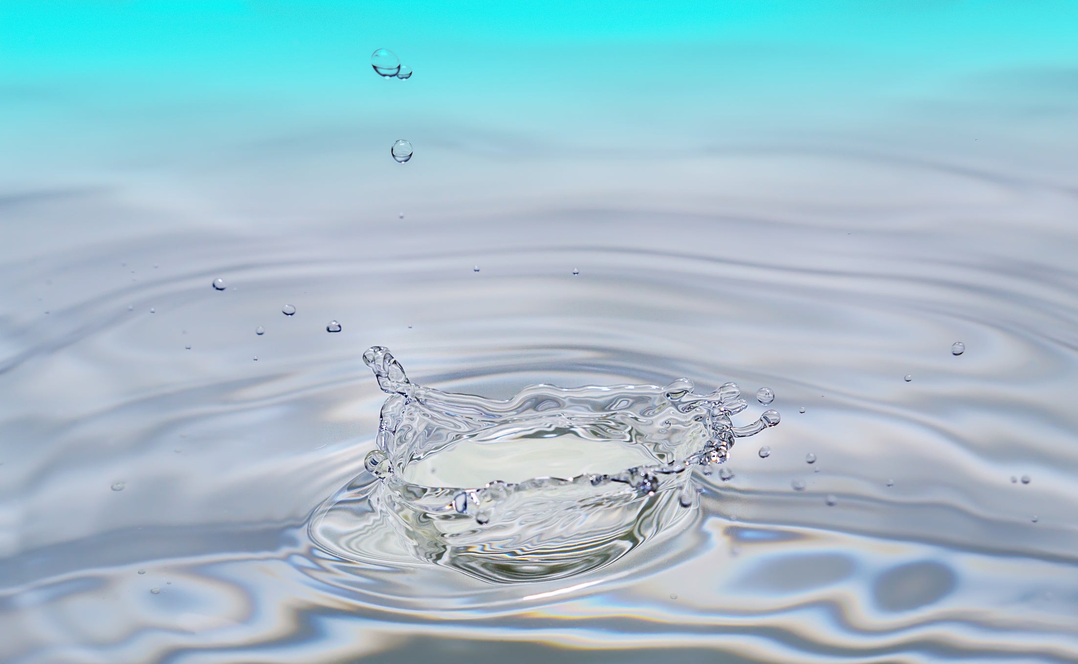 A water droplet falling into a tranquil body of water, creating ripples and splashes