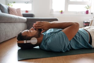 The single man meditating alone at home while listening to meditation music through wireless headphones, doing breathing exercises.