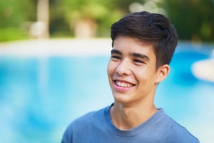 Boy smiling in a yard with a pool in the background.