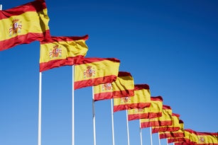 Many Spanish Flag Waving In The Wind In A Row Against Blue Sky.