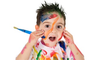 Young child covered in paint holding a paintbrush