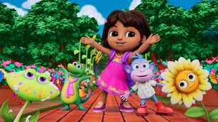 Dora stands on a red brick path with her arms wide open, celebrating with Boots the monkey, Isa the iguana, and two cheerful, smiling flowers. They are all surrounded by a lush green forest and a bright blue sky, looking ready for a fun day of adventure together.