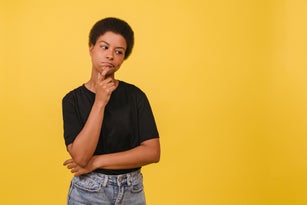 Portrait of thinking young black woman on yellow backdrop