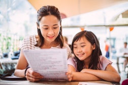 Mom & daughter looking at food menu together in restaurant joyfully