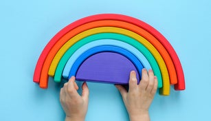 Kids hands playing with wooden toy rainbow on blue background