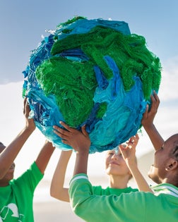 Group of young climate activists holding up a globe together by the sea