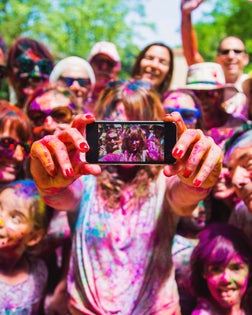 People taking a selfie together in group during a Holi celebration party in the outdoor with happiness expressions and covered with vivid colors.