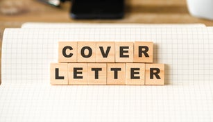 Closeup on notebook over wood table background, focus on wooden blocks with letters making COVER LETTER words