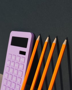Calculator and non-colored pencils on a gray background. Universal gray background. Calculator. Educational supplies.