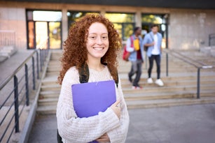 Young redhead female student looking at camera cheerful while standing outside of the high school.