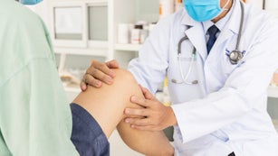 A doctor examines a patient's knee in a medical office setting.