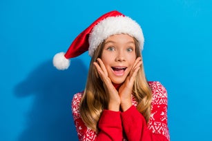 Portrait of overjoyed teen girl wear jumper santa hat hold palms on cheekbones astonished staring isolated on blue color background